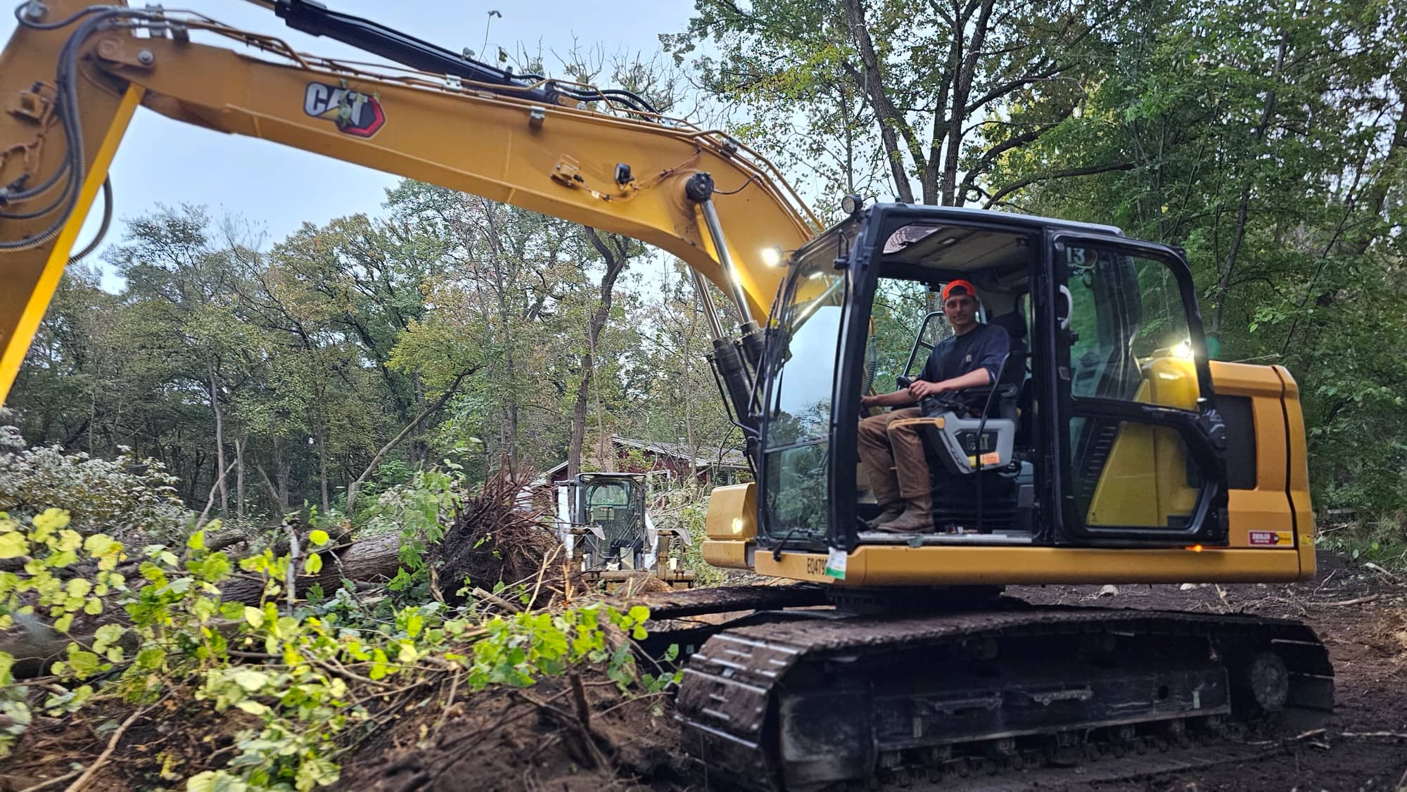A CAT excavator with its operator at work, trees in the background